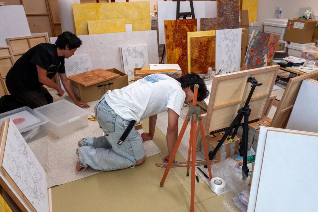 制作途中の作品が並ぶアトリエで、二人の作り手が作業している様子